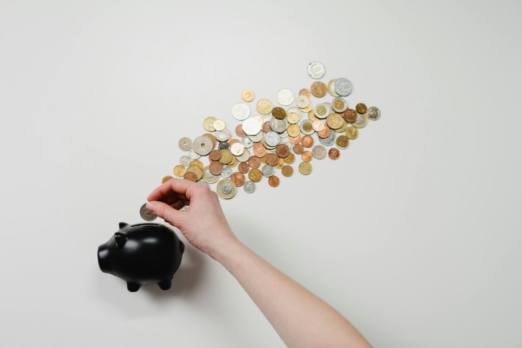 Sparen am falschen Ende: Warum gekürzter Brandschutz teuer werden kann Person placing coin into a black piggy bank with scattered coins, symbolizing savings and finance.