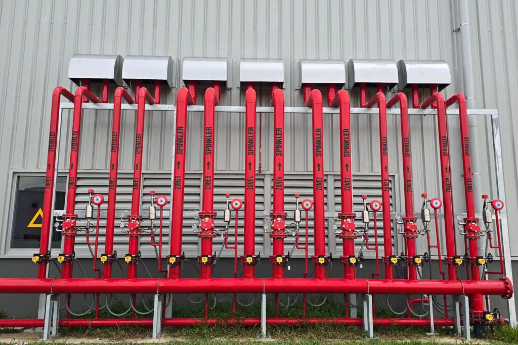 Red industrial fire sprinkler pipes aligned on a factory exterior wall.